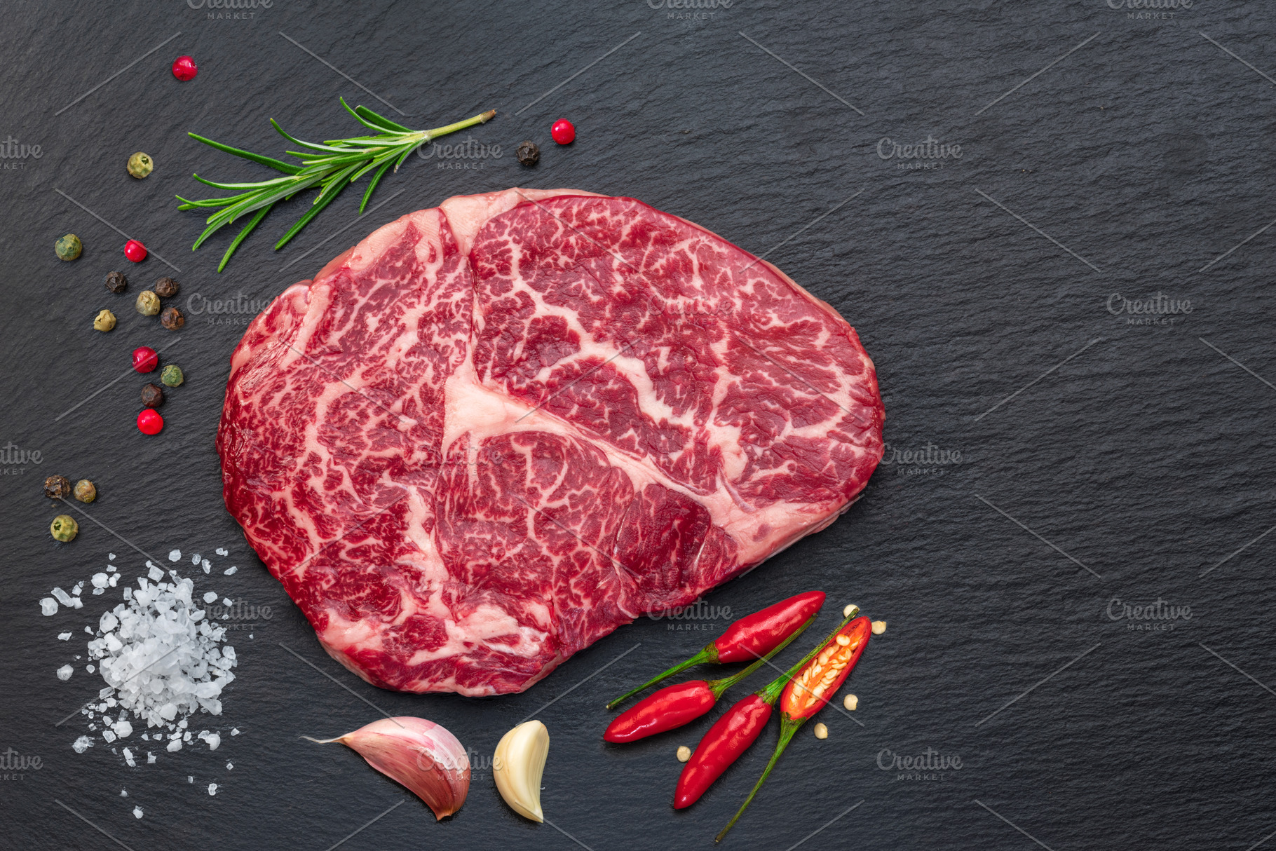 Raw ribeye steak on stone black serving plate. Flat lay., a Food & Drink Photo by Volff