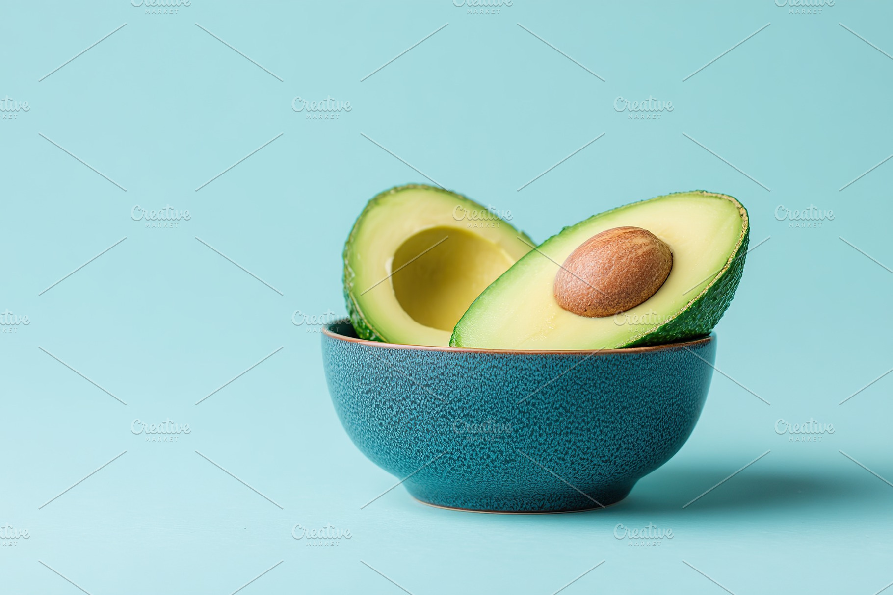 Freshly cut avocado half with seed showcased in a bowl against a vibrant blue b, a Food & Drink Photo by AlyaAnd