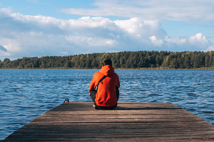 A young man in a bright orange hoodie on a wooden pier against the background o, a Person Photo by PavelKant