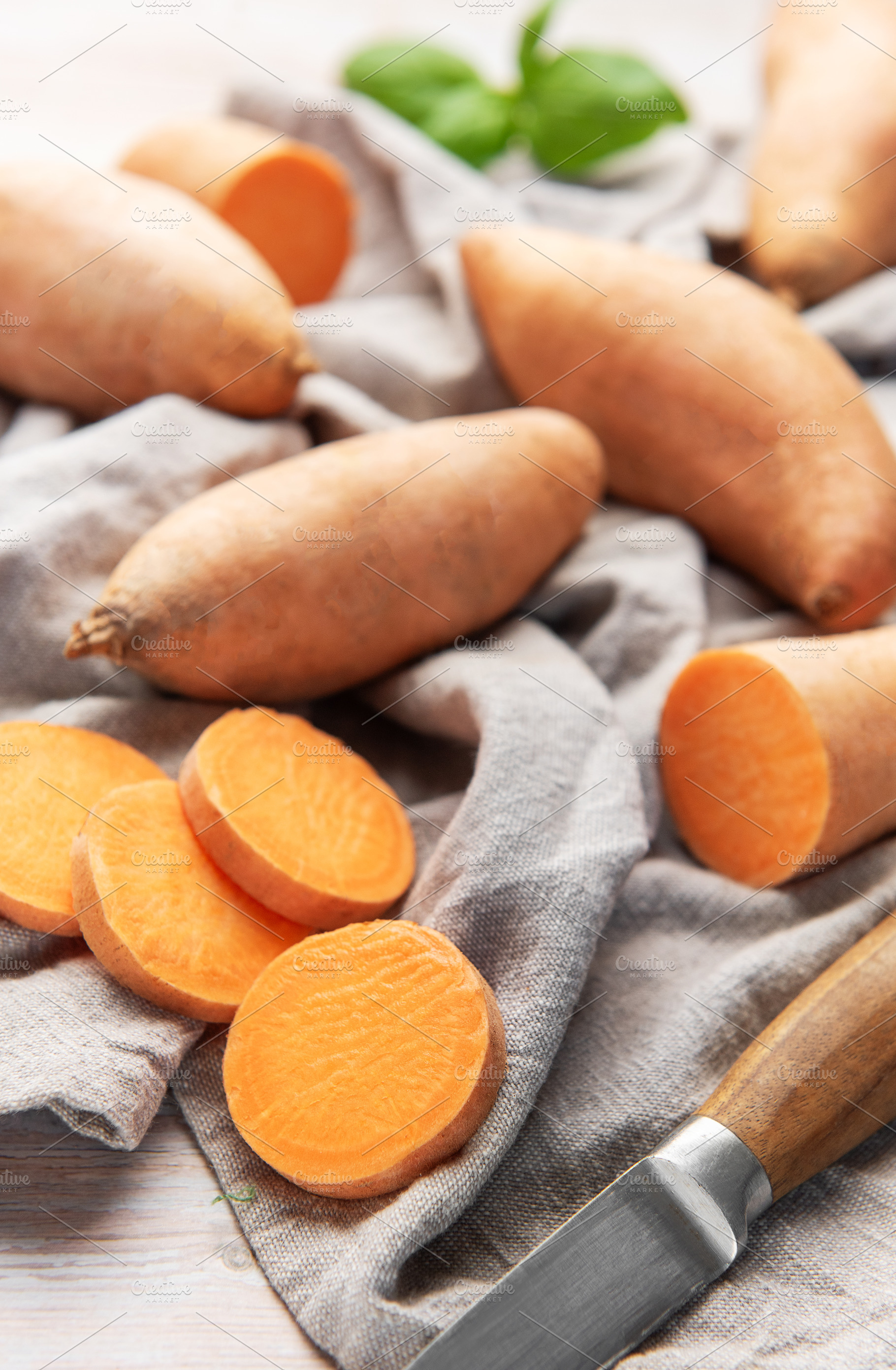 Raw sweet potatoes with sliced pieces and knife for cooking, a Food & Drink Photo by Olena Rudo