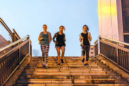 Women friends training running down stairs in town on sunset