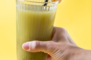 Hand holding a green smoothie with banana on a yellow background, a Food & Drink Photo by etorres69