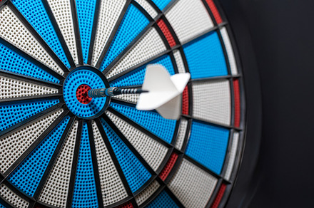 Close-up of a white dart perfectly striking the red bullseye on