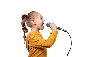 Joyful young girl in a yellow sweater singing into a microphone, a Person Photo by Ales Munt