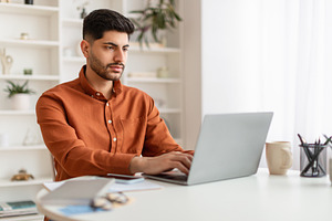 Arab man using laptop sitting at desk in office, a Photo by Prostock-Studio