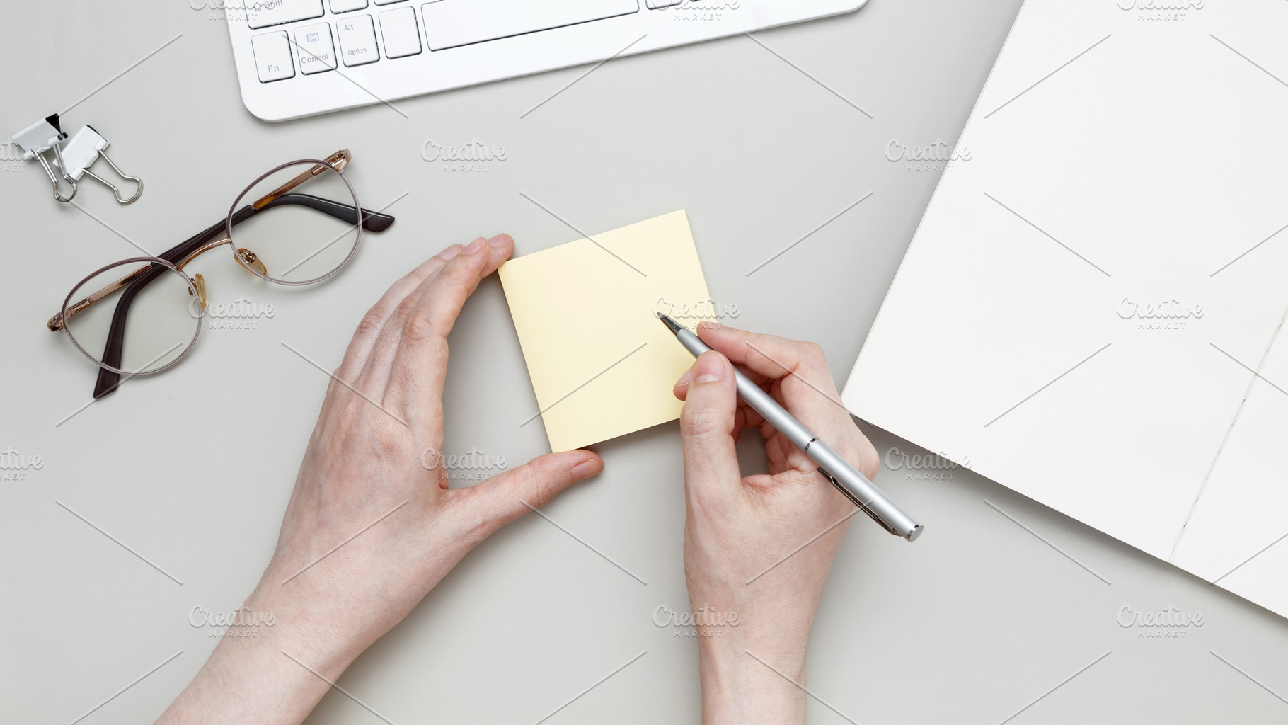 At tidy workspace, woman jots notes on sticky pad surrounded by notebook and st, a Photo by matucha