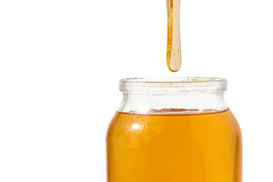 Liquid honey dripping from a wooden honey spoon into a glass jar, a Food & Drink Photo by ndanko
