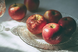 Fresh Gala apples sitting on a clear glass plate, receiving gent, a Photo by Studio ANNA