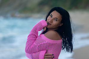Confident woman with dark hair in a pink sweater poses on a sandy beach with wa, a Person Photo by Ales Munt