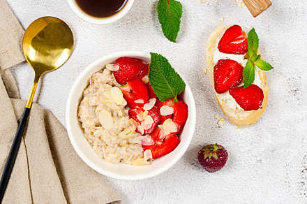 A bowl of oatmeal with strawberries and almond flakes on a table, a Food & Drink Photo by vimart
