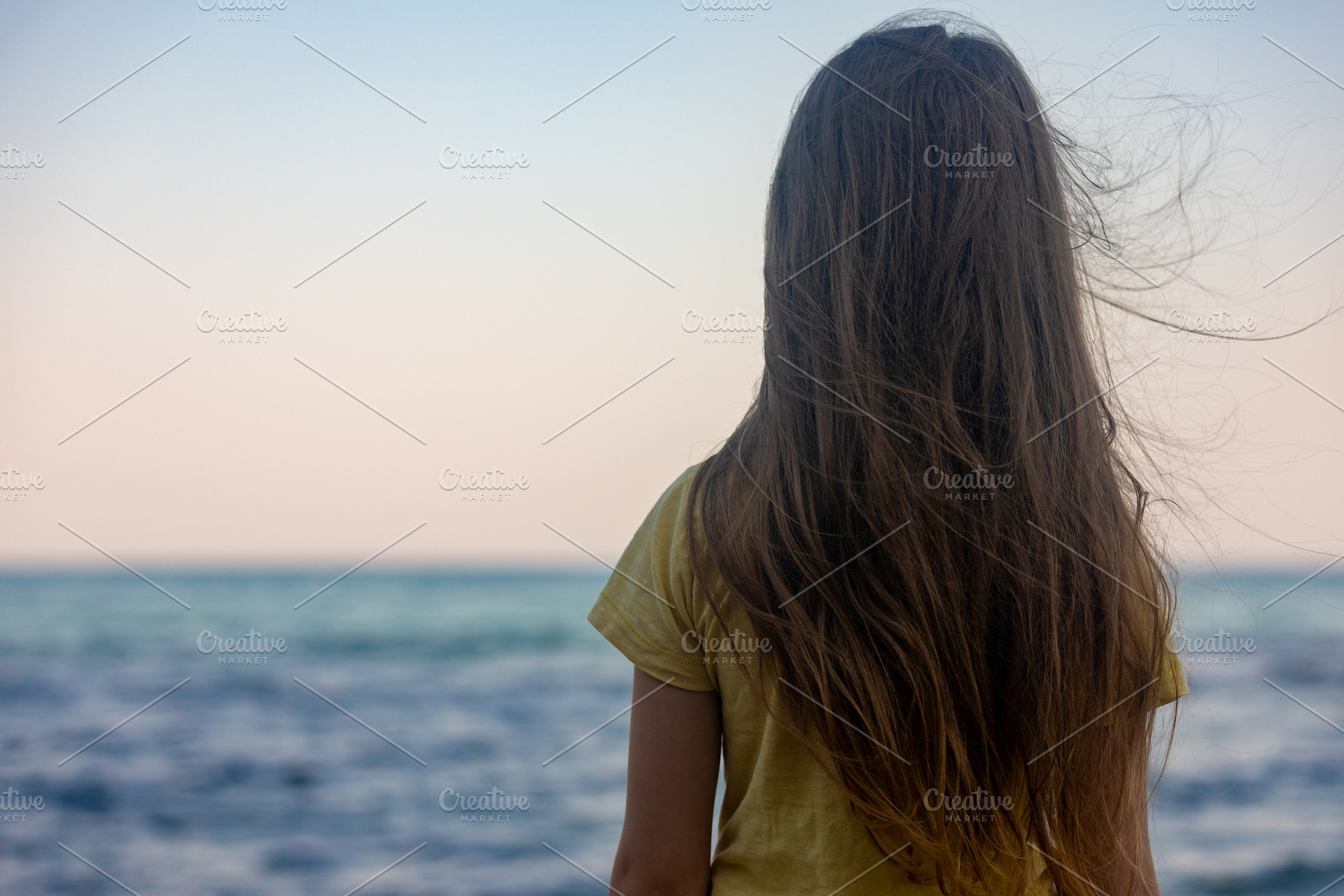 Young girl with long hair standing on the beach, gazing at the calm ocean under, a Person Photo by Ales Munt