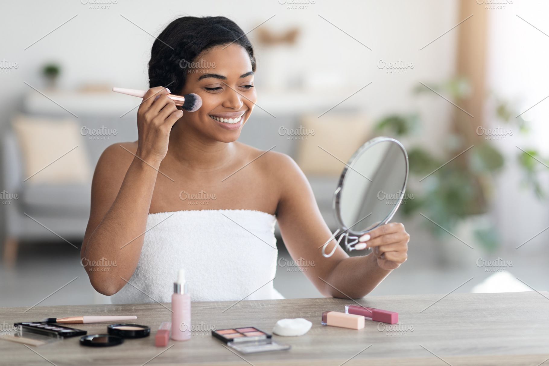 Pretty african american woman wrapped in towel putting make up, a Photo by Prostock-Studio