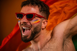 Excited man celebrating pride with rainbow flag and face paint, a Photo by karrastock