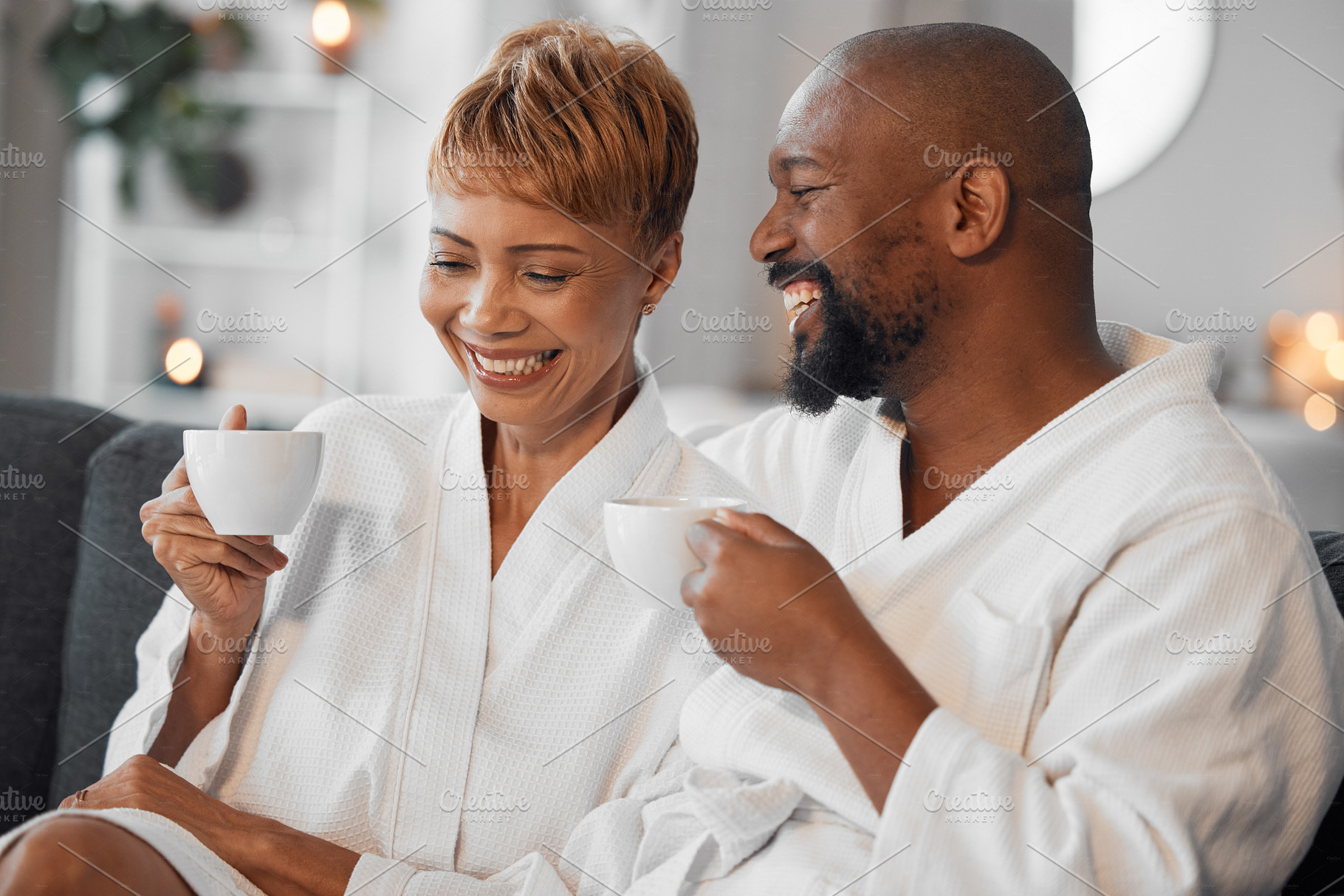 Coffee, love and mature couple on a sofa, happy and laughing while drinking coffee and relax in bathrobe in living room. Black family, tea and senior man and woman enjoy morning conversation on couch, a Photo by Peopleimages.com