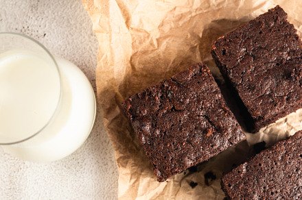 Chocolate brownie on paper and glass of milk on dark stone table, a Food & Drink Photo by vimart