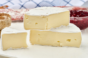 Sliced round head of Camembert cheese on a white board and, a Food & Drink Photo by ndanko