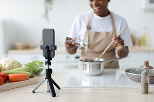 Satisfied millennial black lady in apron cooking at home shooting video lesson, a Person Photo by Prostock-Studio