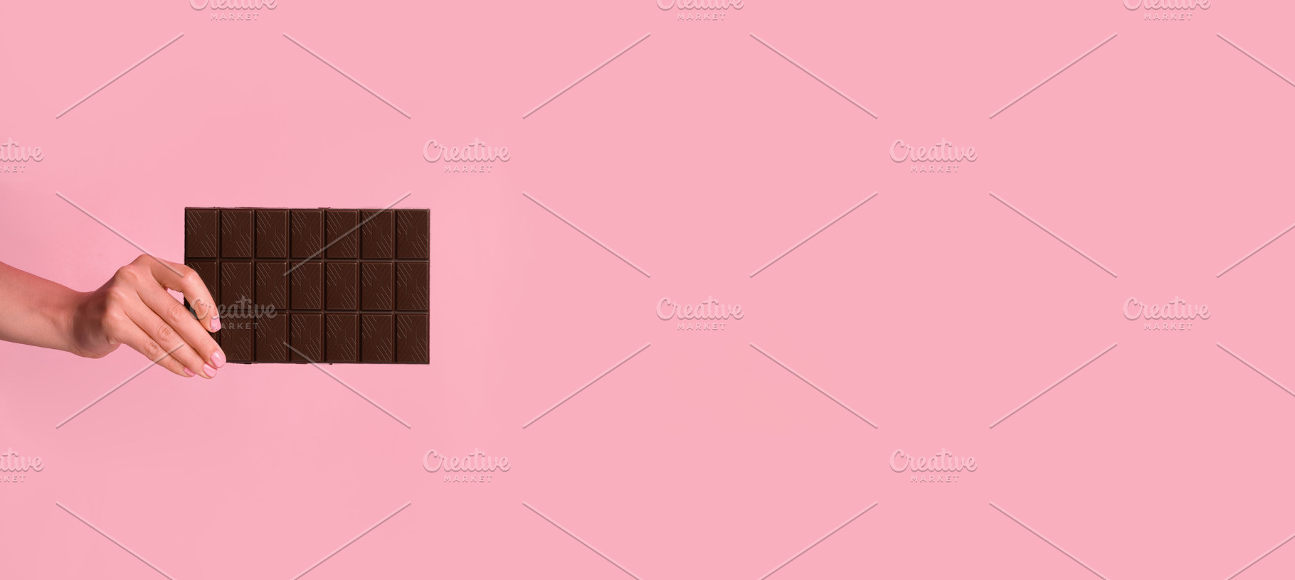 Woman’s hand holding a dark chocolate bar on soft pink backgro, a Food & Drink Photo by Ales Munt