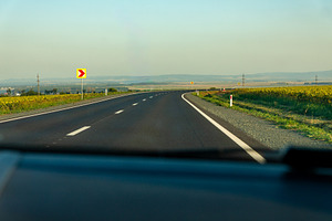 Wide view of a rural highway curving through open countryside under a clear sky, a Transportation Photo by Ales Munt