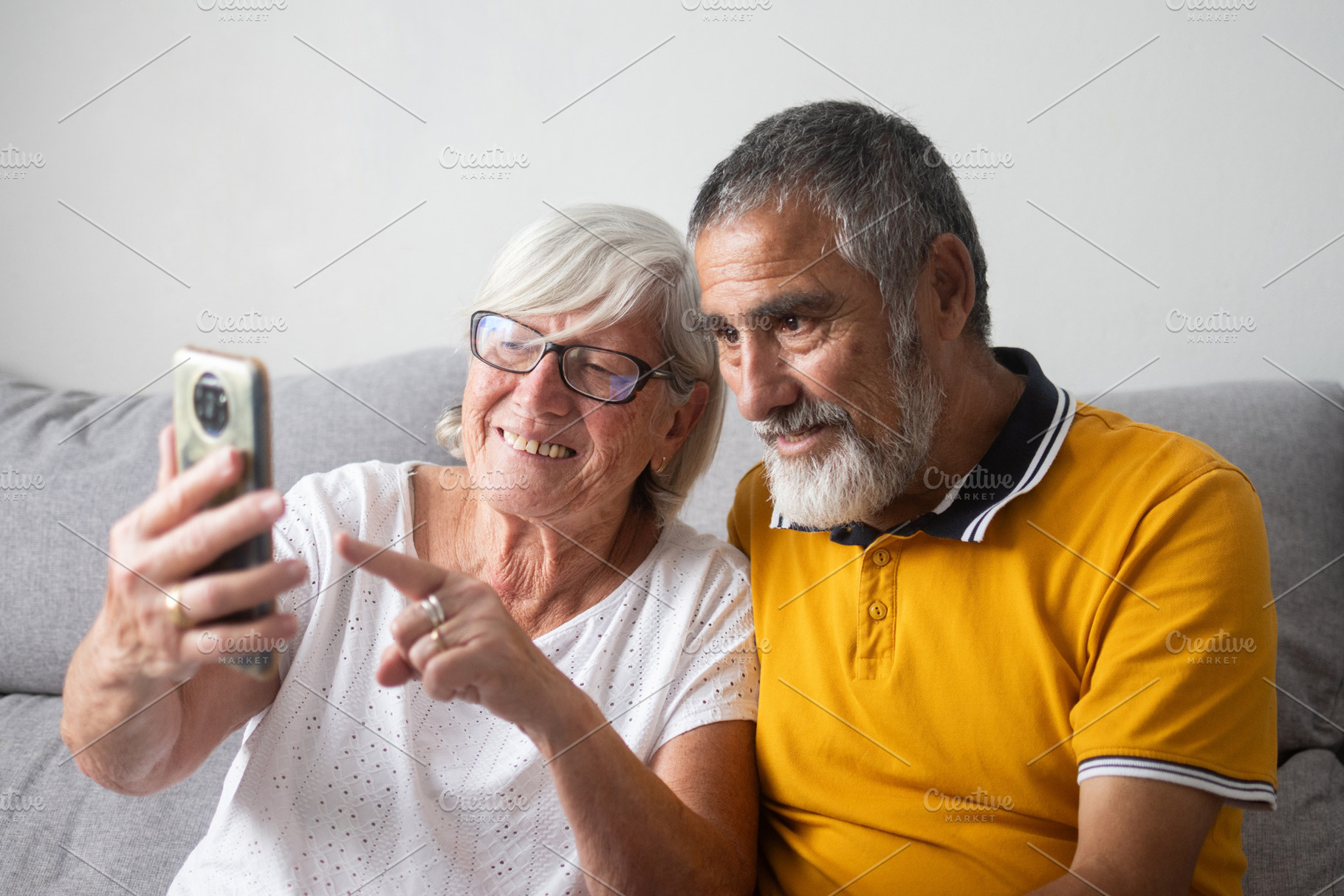 Happy senior couple looking at smartphone together on sofa, a Person Photo by etorres69