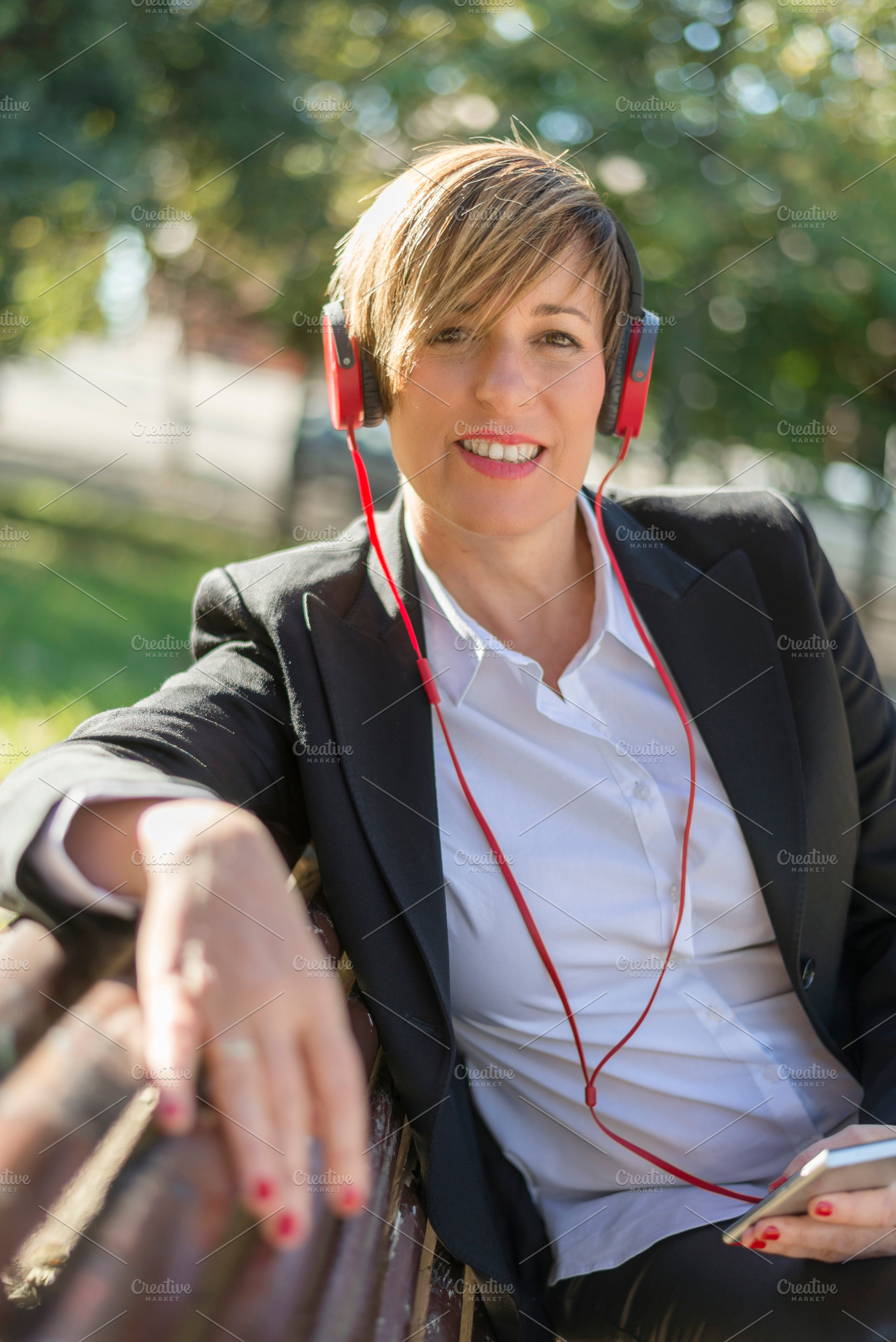 Smiling businesswoman with red headphones outdoors, a Photo by RF Images
