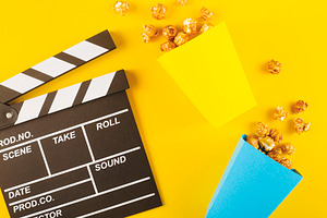 Popcorn and clapperboard on yellow