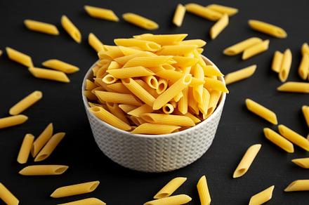 Organic Dry Penne Pasta in a Bowl on a black background, side vi, a Food & Drink Photo by LiudmylaChuhunova