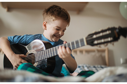 Happy boy playing on the guitar in, a School & Education Photo by HalfPoint