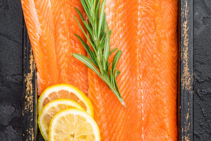 Uncooked salmon fillet with bright orange flesh rosemary and lem