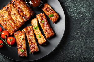 Hot grilled spare ribs from a summer BBQ served on a plate with sauce. Top view, a Food & Drink Photo by Budarinphoto