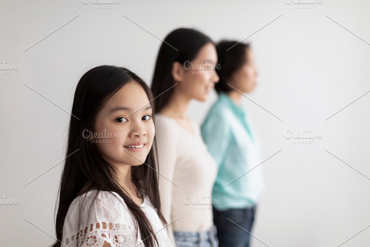 Cheerful little Asian girl with her mother and grandmother posing on white stud, a Photo by Prostock-Studio (Photo 2 of 2)