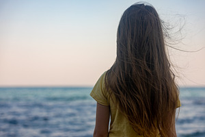Young girl with long hair standing on the beach, gazing at the calm ocean under, a Person Photo by Ales Munt