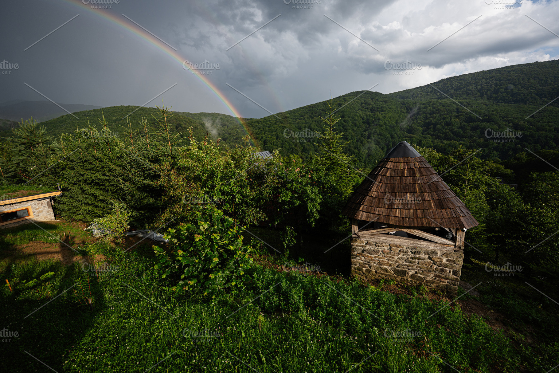 Rustic hut and rainbow in lush green countryside under moody sky, a Photo by AS photostudio