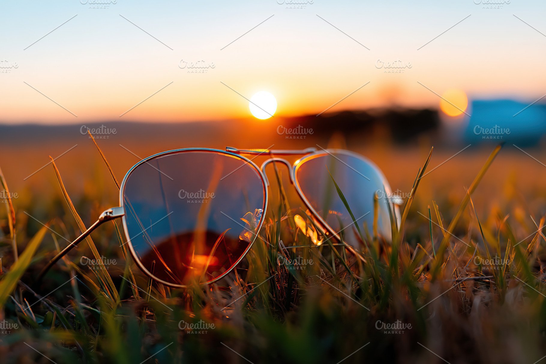 Sunglasses on grass during sunset with warm hues illuminating the evening sky, a Beauty & Fashion Photo by AlyaAnd