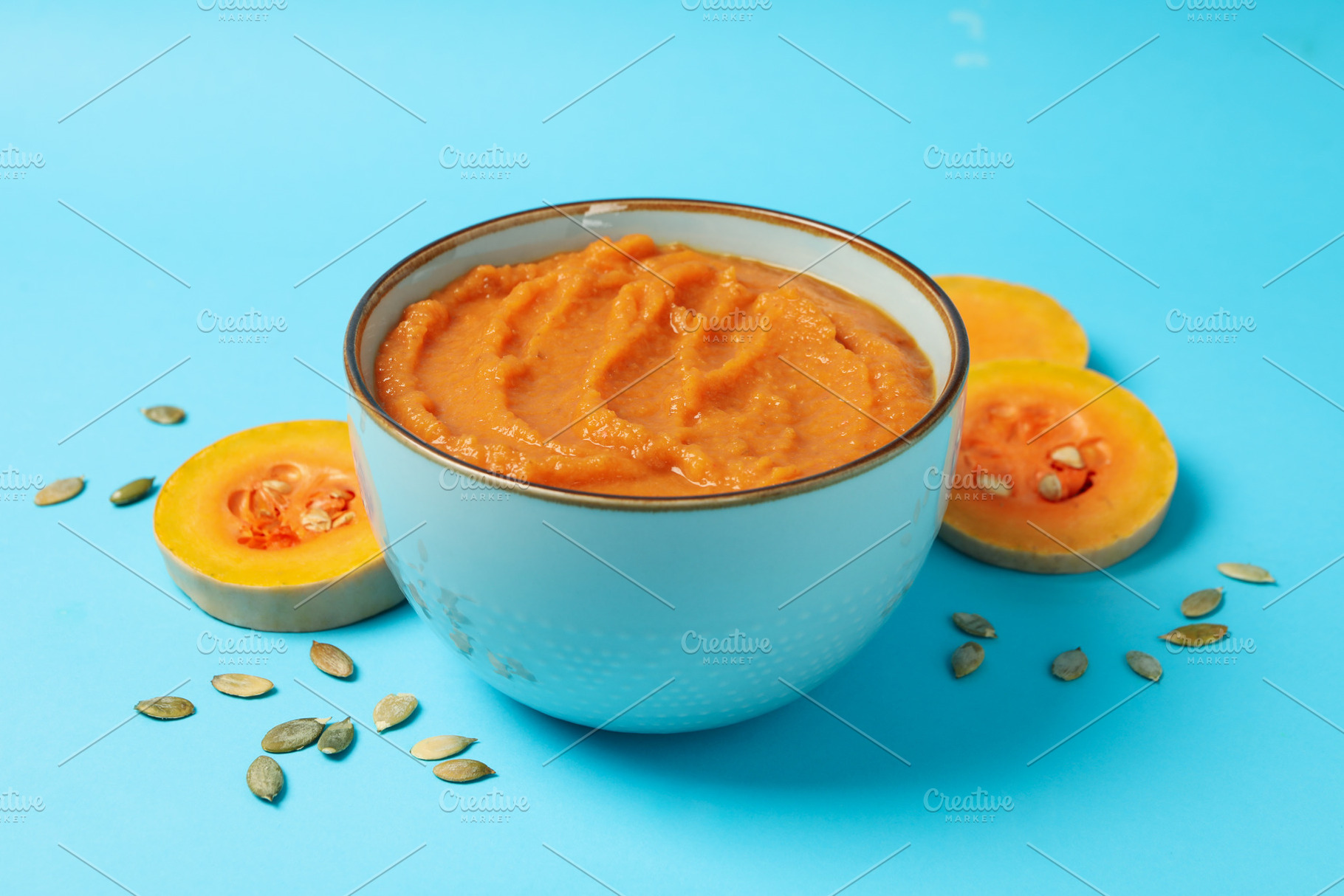 Bowl of pumpkin puree, seeds and slices on blue background, clos, a Food & Drink Photo by AtlasStudio PRO