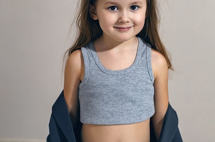 funny portrait of a fashionable girl child in a large gray jacket stands agains, a Person Photo by SaulichPhoto