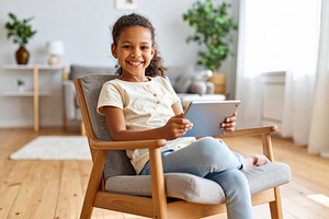 Girl with a tablet sitting on chair at living room while smiling, a Person Photo by DanFLCreativo