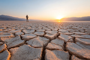 Cracked earth landscape at sunset with figure standing in vast desert expanse, a Photo by AlyaAnd