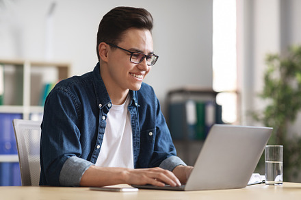 Handsome young businessman in glasses working with laptop in modern office, a Photo by Prostock-Studio