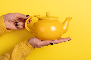 Close-up of a yellow teapot held in hands against a matching yel, a Food & Drink Photo by Ales Munt