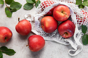 Fresh red apples spilling from reusable mesh bag on table, a Food & Drink Photo by Olena Rudo