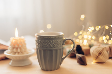 Cozy winter still life. Mug with tea or coffee, burning candle, book, gift box