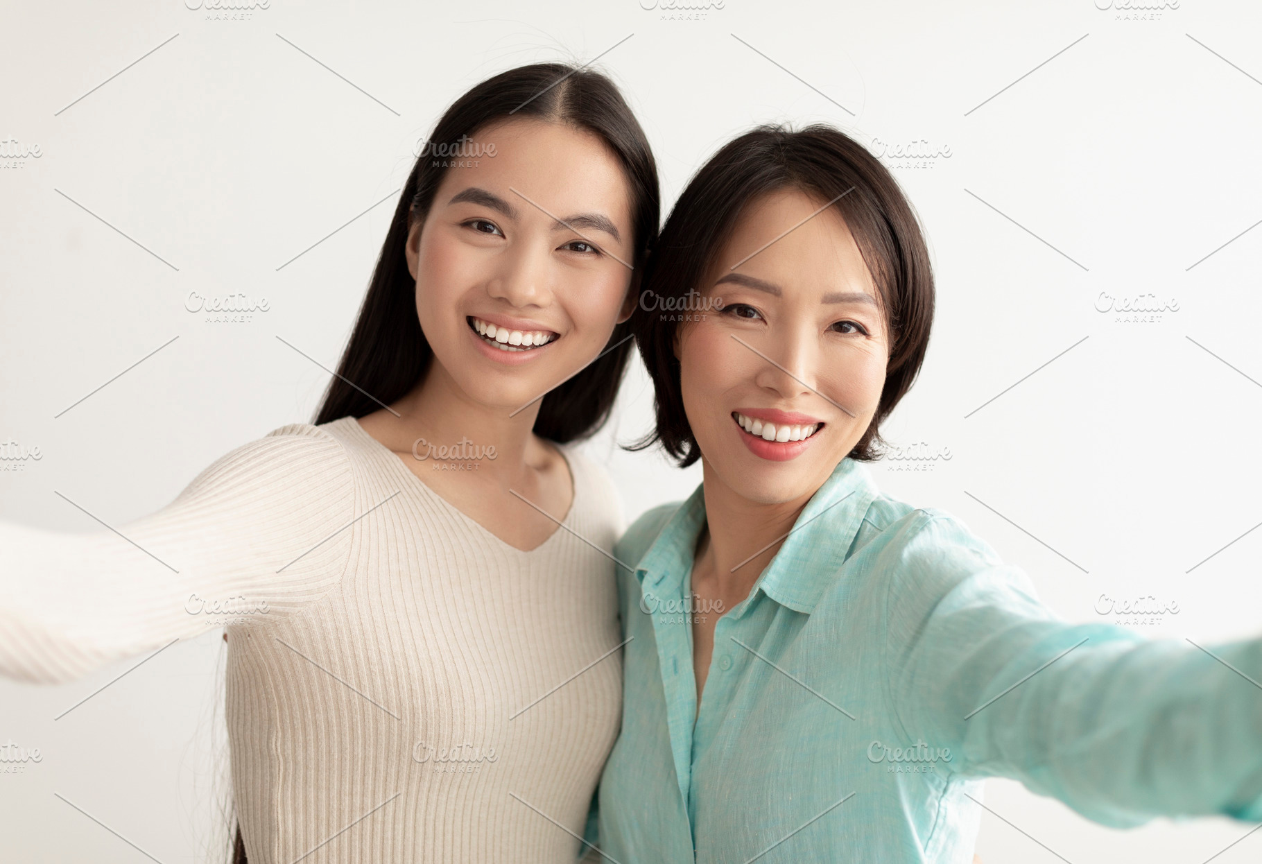 Happy young Asian woman and her mature mother taking selfie together on white s, a Photo by Prostock-Studio