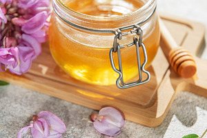 Acacia honey jar with blooming flowers and wooden dipper, a Food & Drink Photo by Olena Rudo