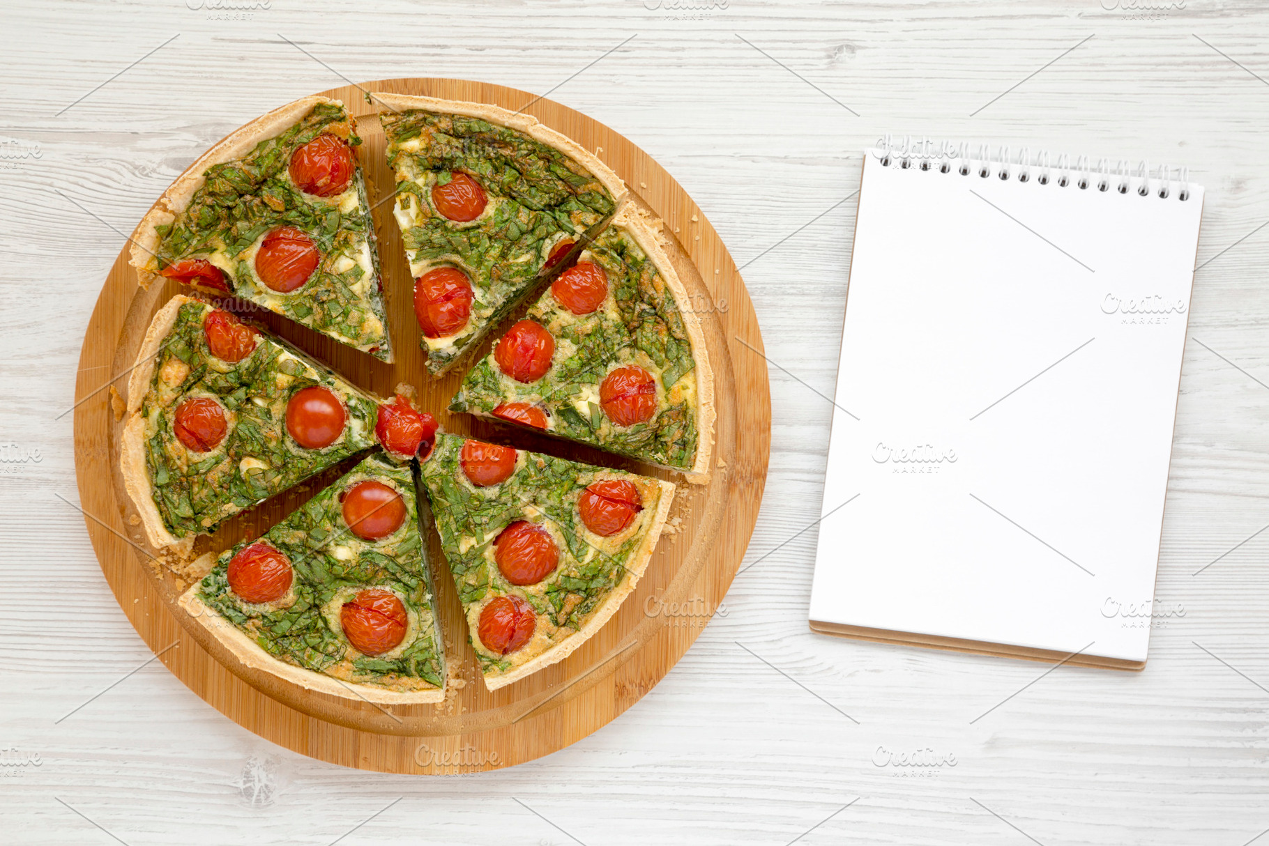Homemade Spinach Quiche on a round bamboo board, blank notepad o, a Food & Drink Photo by LiudmylaChuhunova