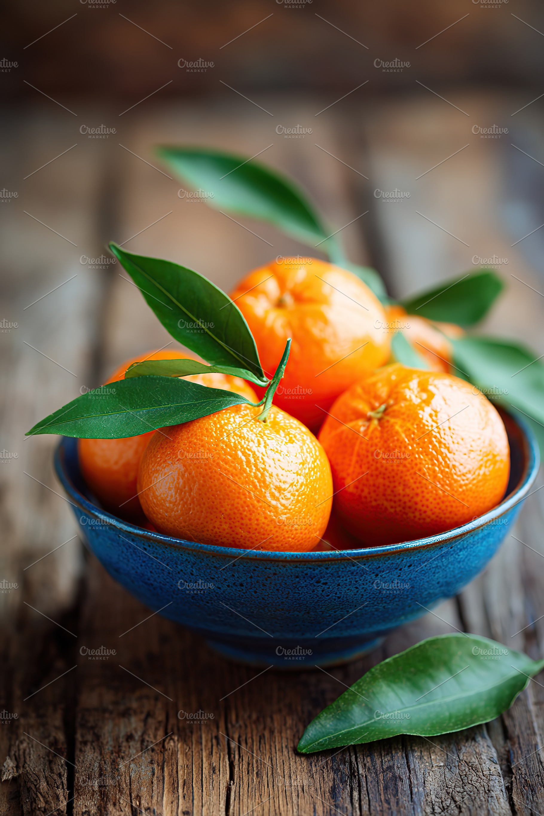 Fresh mandarins in a blue bowl with green leaves on a rustic wooden table, a Food & Drink Photo by AlyaAnd