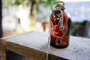 Decorative amber bottle with rope and rooster design placed on wooden surface, a Photo by AS photostudio