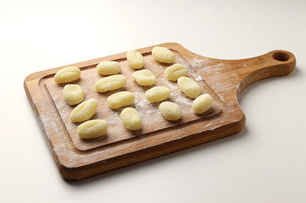 Cutting board with raw potato gnocchi on white background, a Food & Drink Photo by AtlasStudio PRO