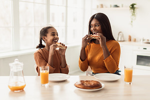 African Mother And Daughter Having Lunch Eating Sandwiches In Kitchen, a Photo by Prostock-Studio