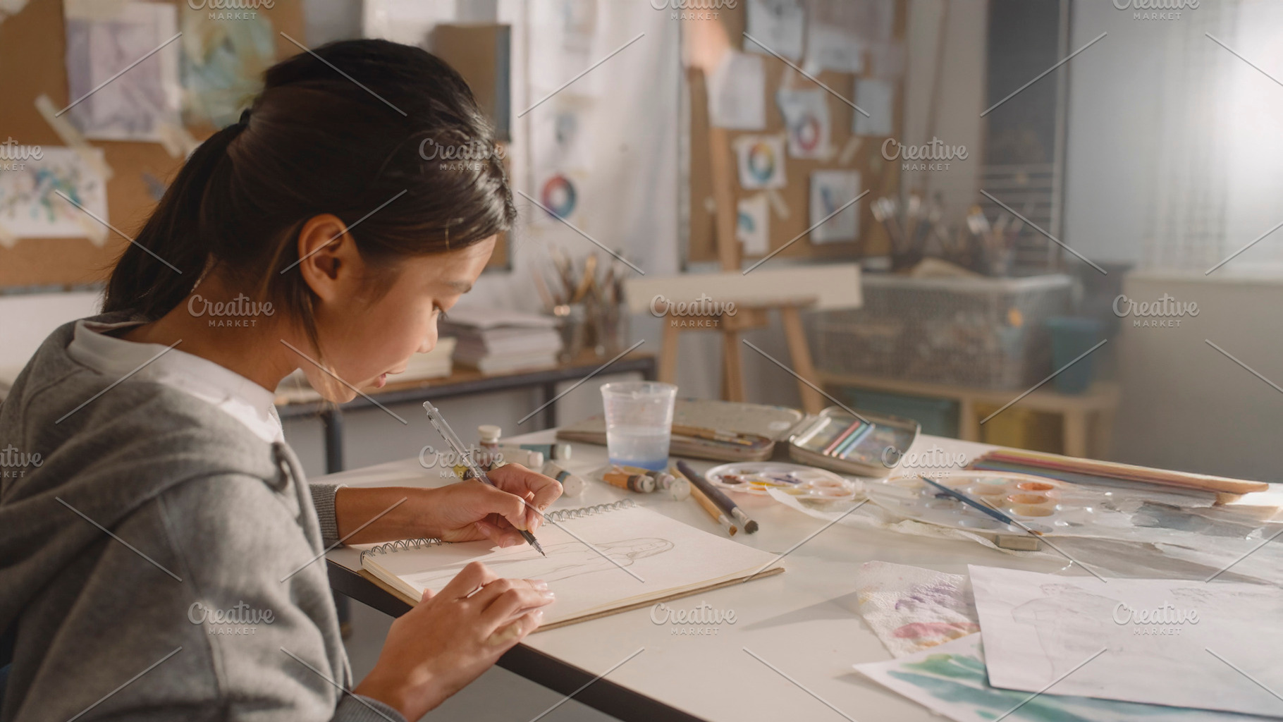 Asian teenager adding details to a sketchbook during an art clas, a School & Education Photo by DanFLCreativo